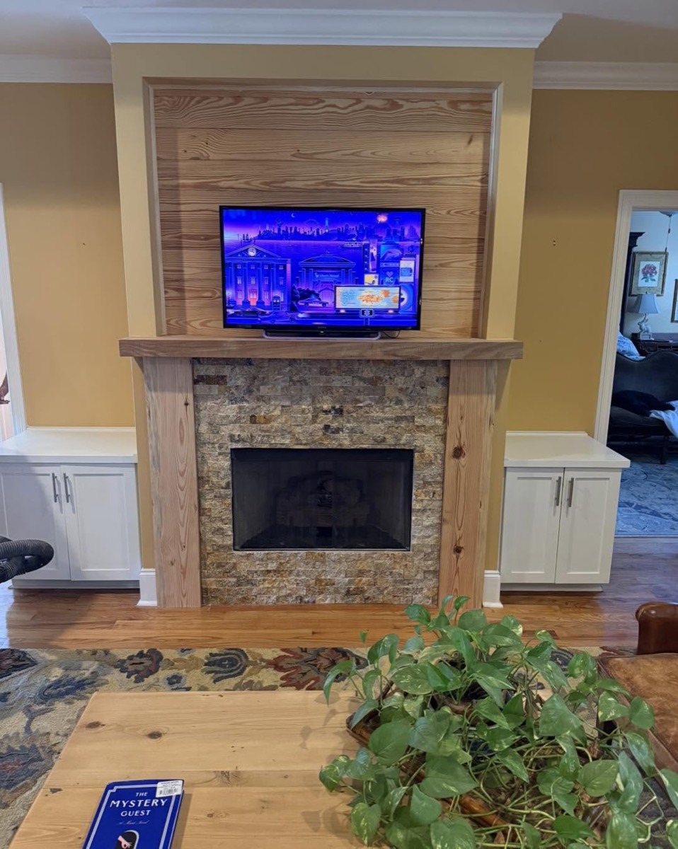 Living room with a TV mounted above a stone fireplace flanked by built-in white cabinets