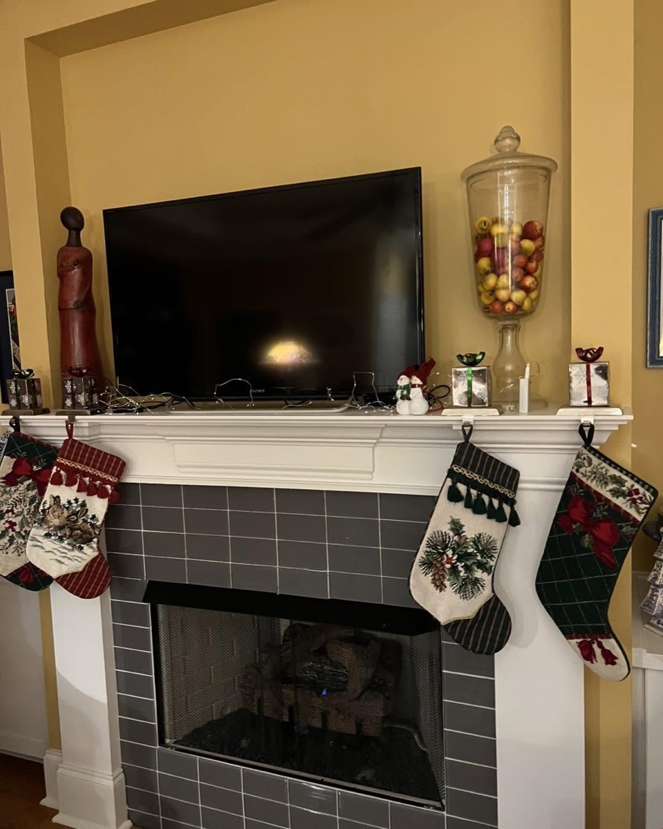 Television mounted above a white mantel and brick fireplace decorated for the holidays