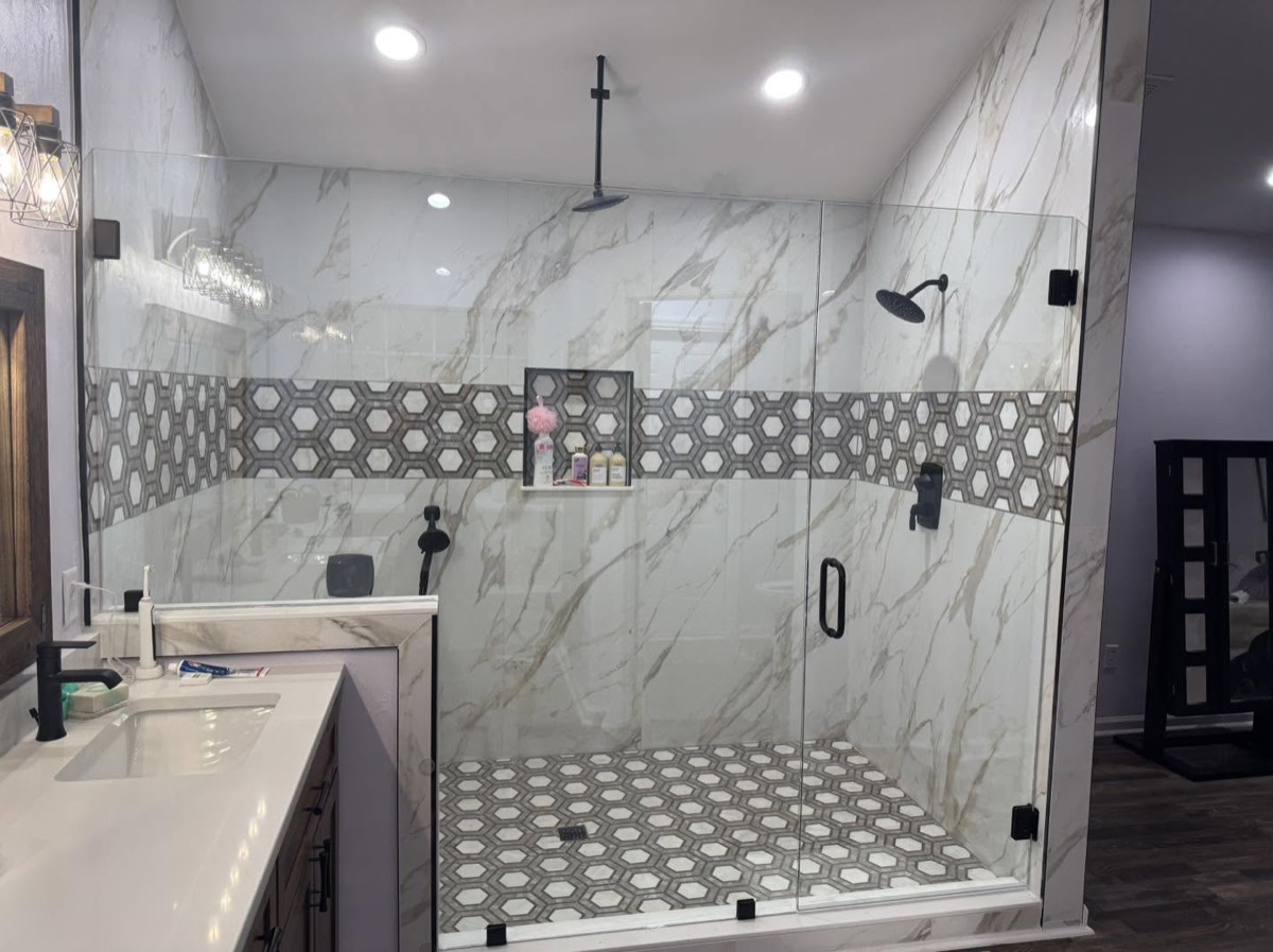 Walk-in shower with marble-look tile, a hexagon tile accent band, black fixtures and a glass door