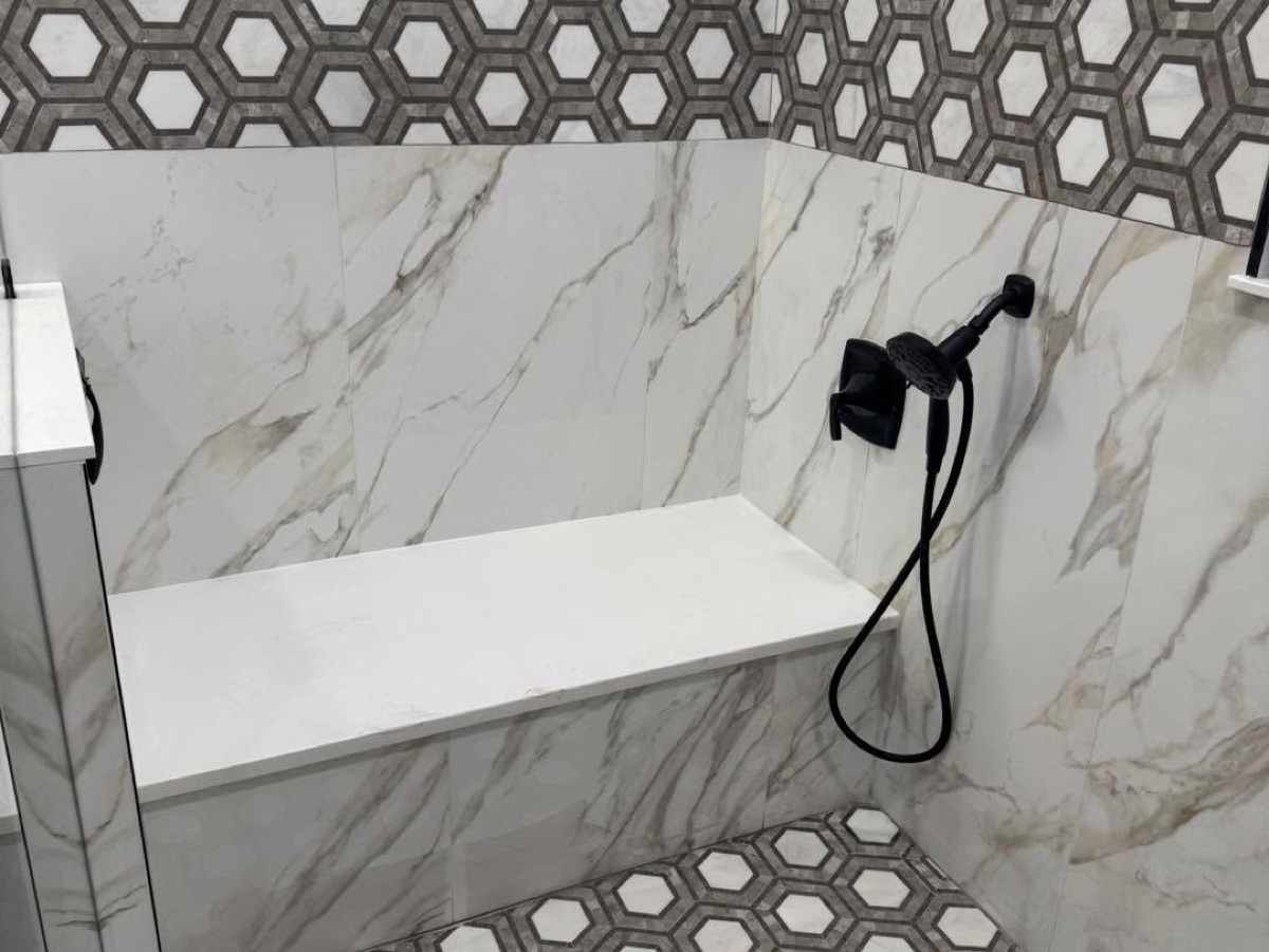 Close view of a tiled shower bench with hexagon floor tile and black hand shower