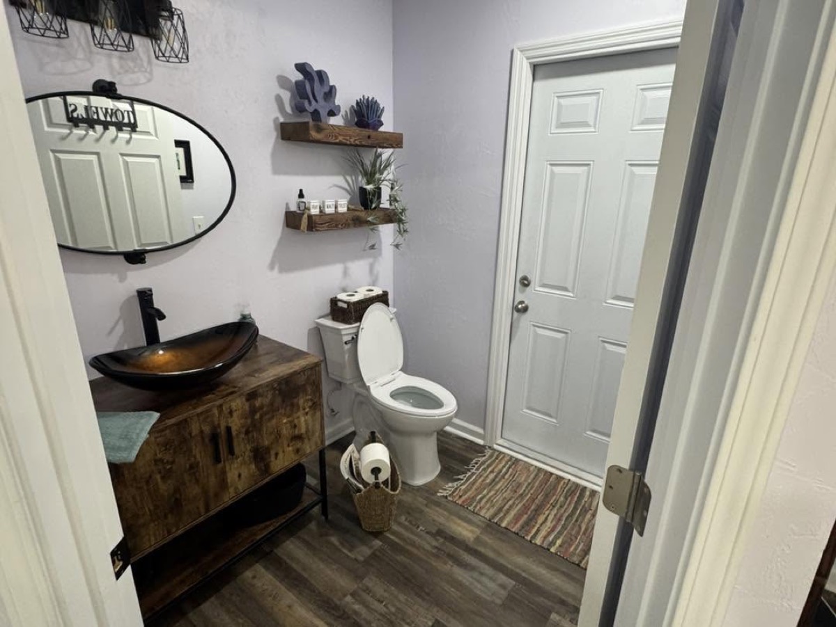 Powder room with a copper vessel sink on a rustic wood vanity, round mirror and plank floor