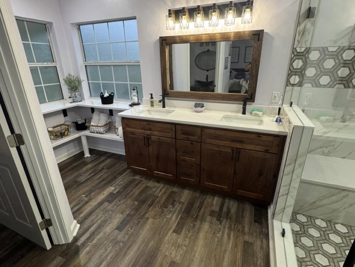 Remodeled bathroom with a dark wood double vanity, white counters, large mirror and wood-look plank floor