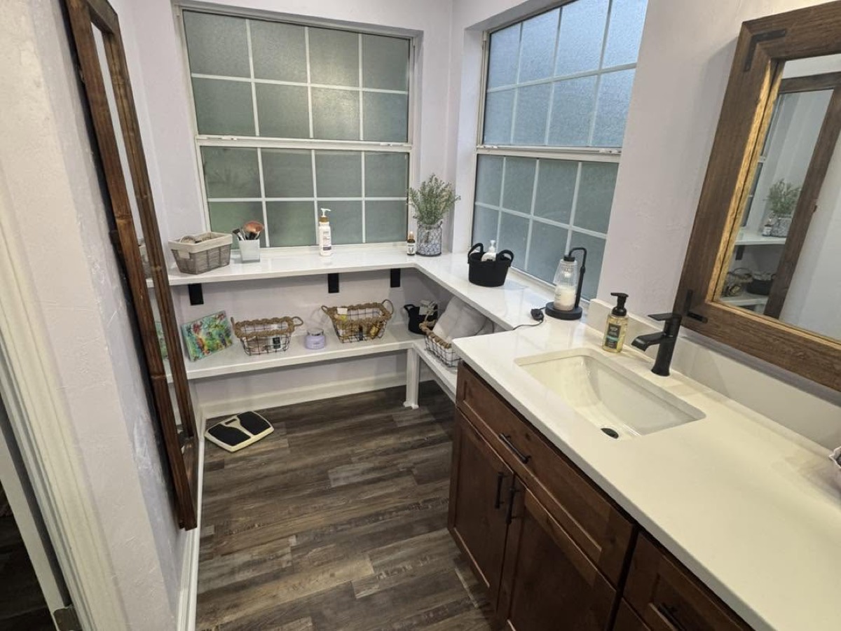 Bathroom vanity with white quartz top under a bright window, wood-look plank floor