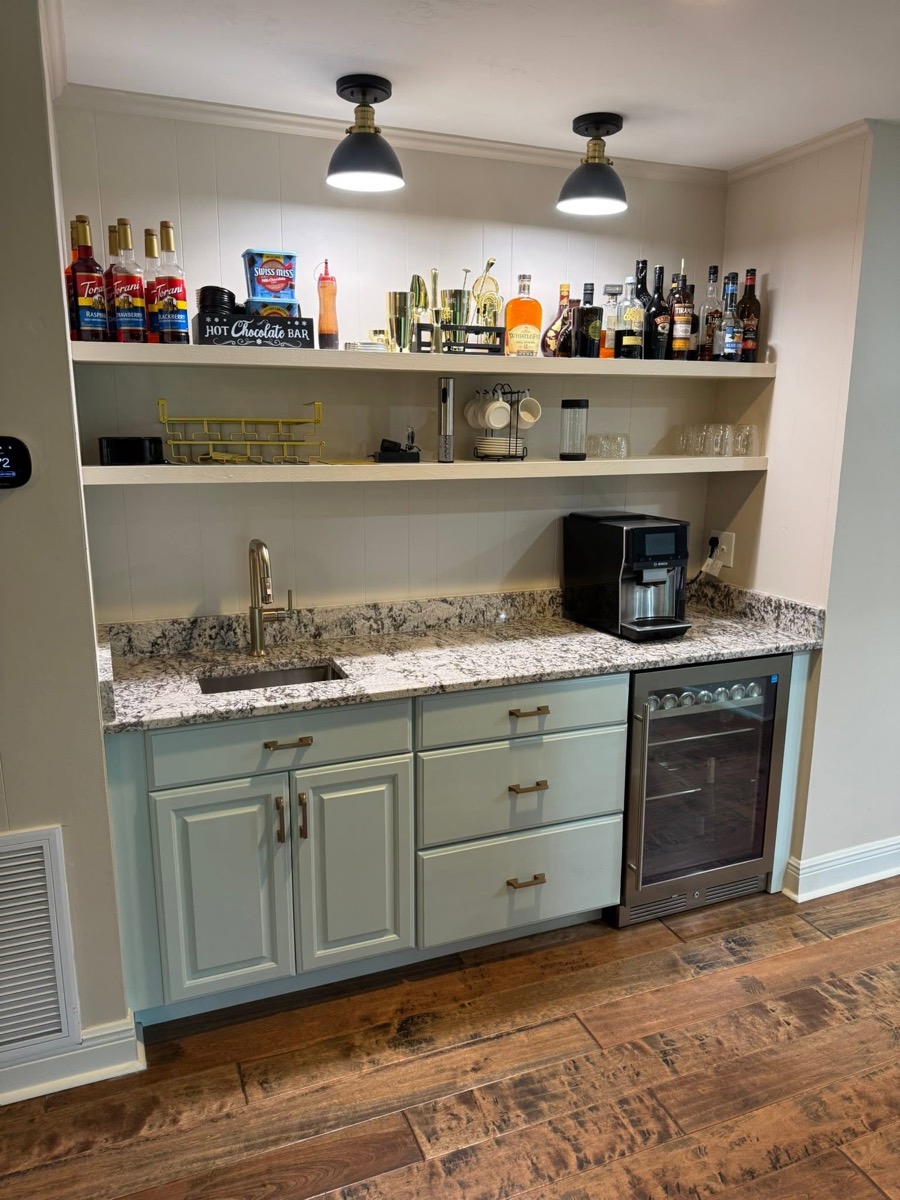 Finished wet bar with pale green cabinets, granite counter, open shelving and a beverage fridge