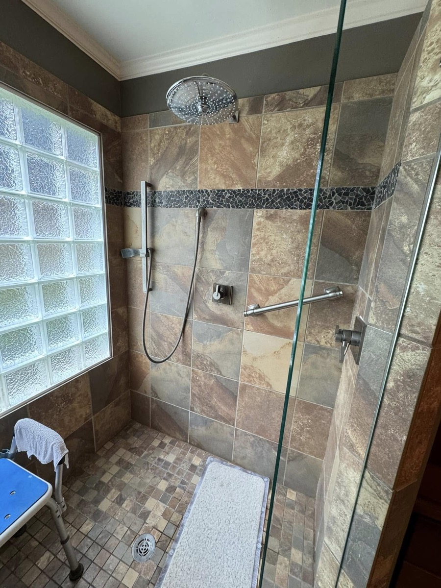 Old walk-in shower with slate tile, a glass block wall and bronze fixtures