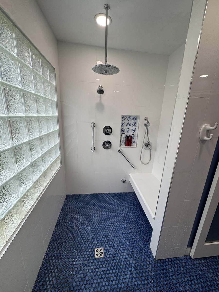 Finished walk-in shower with a rain head, hand shower and grab bar, white tile walls and blue penny-tile floor