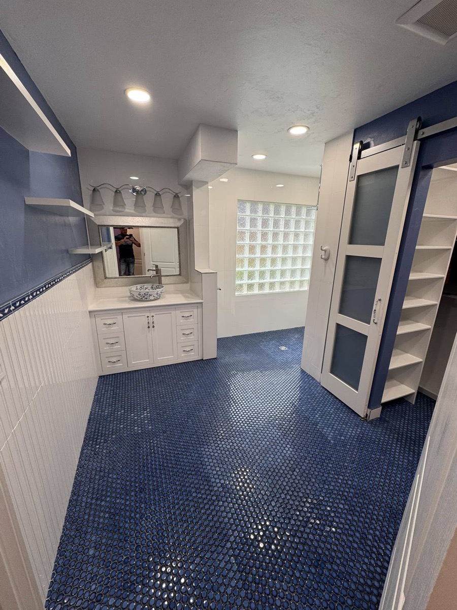 Finished accessible bathroom with white vanity, blue penny-tile floor and a barn door