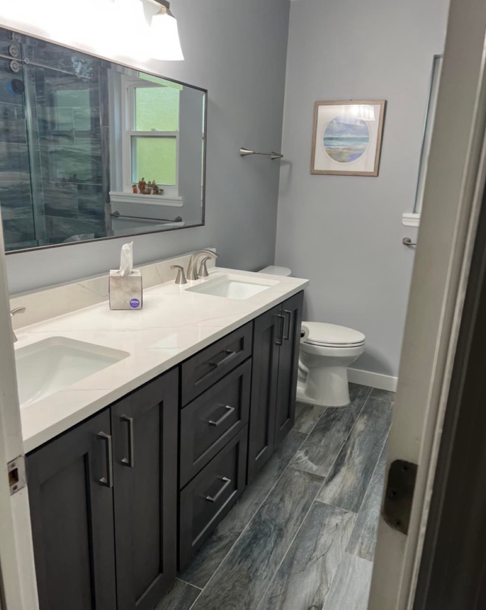 Updated bathroom with a dark double vanity, white quartz top, and grey plank tile floor