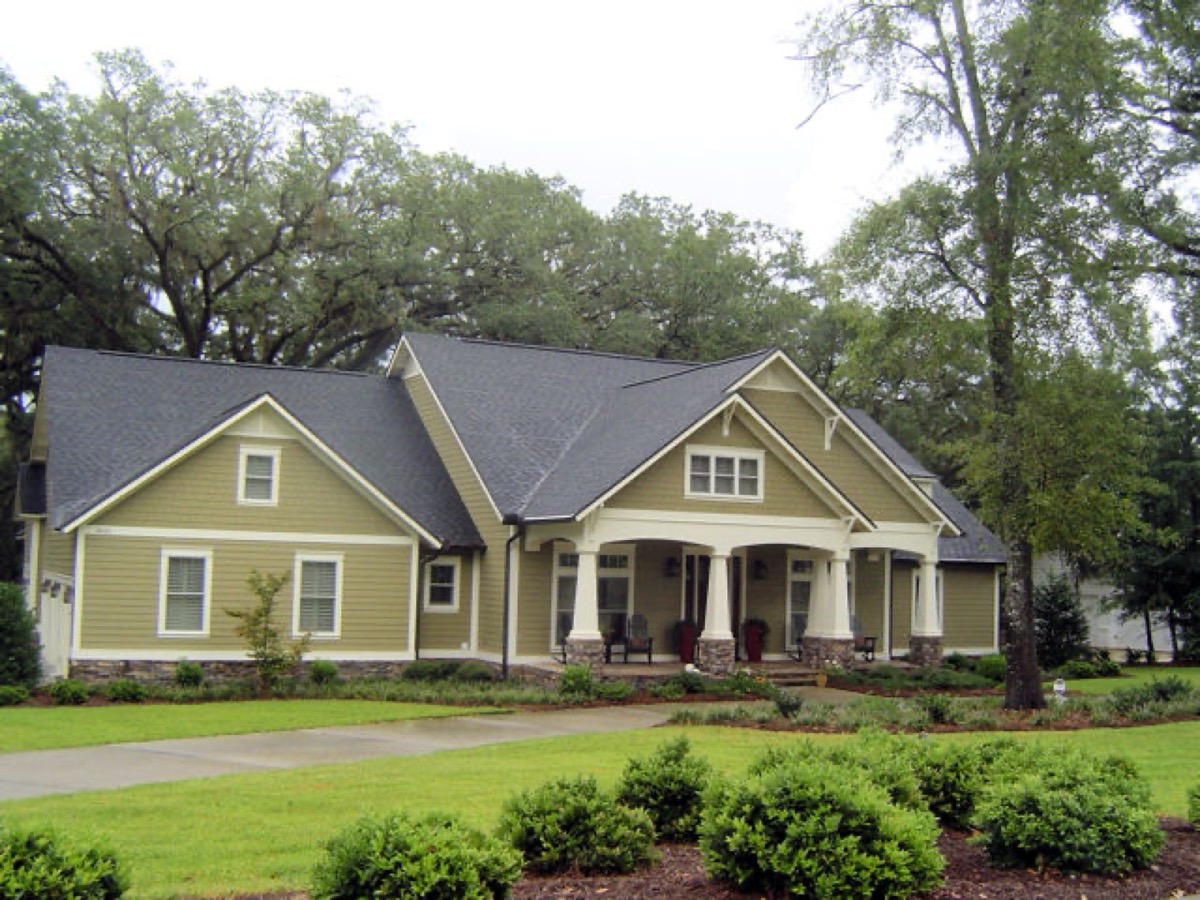 Green craftsman-style home with a covered porch and fresh landscaping