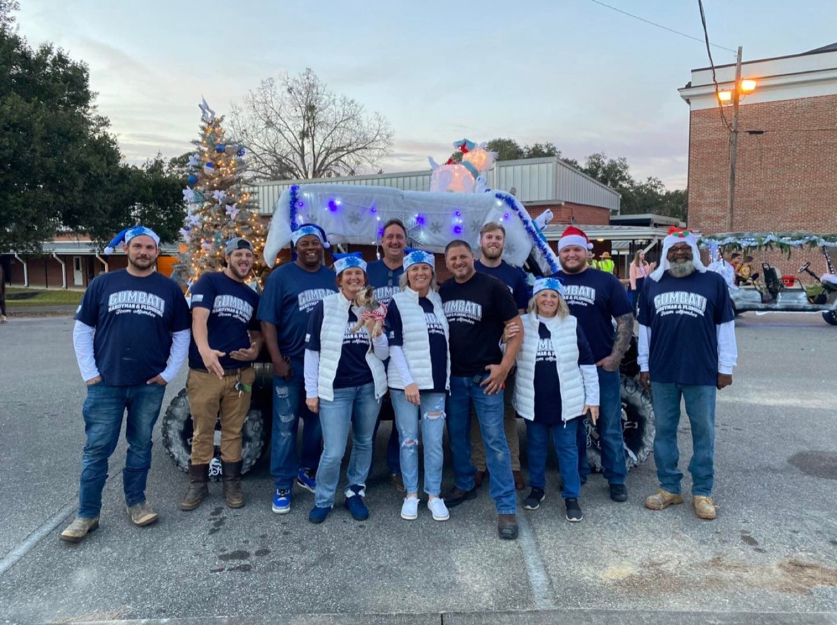 The full Gumbati team, crew and office staff, in matching navy shirts and Santa hats in front of a decorated truck