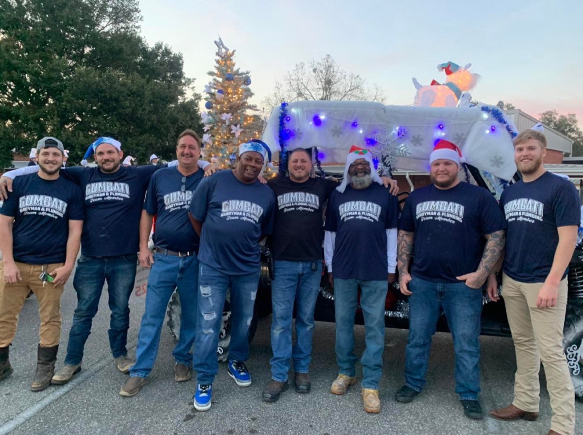 Eight members of Team Gumbati in matching navy shirts in front of a decorated work truck at a holiday parade